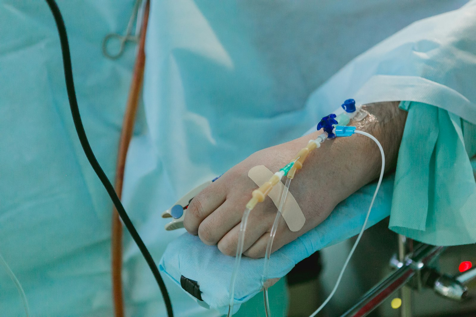 A hand with an infusion line taped in place, resting on a hospital sheet