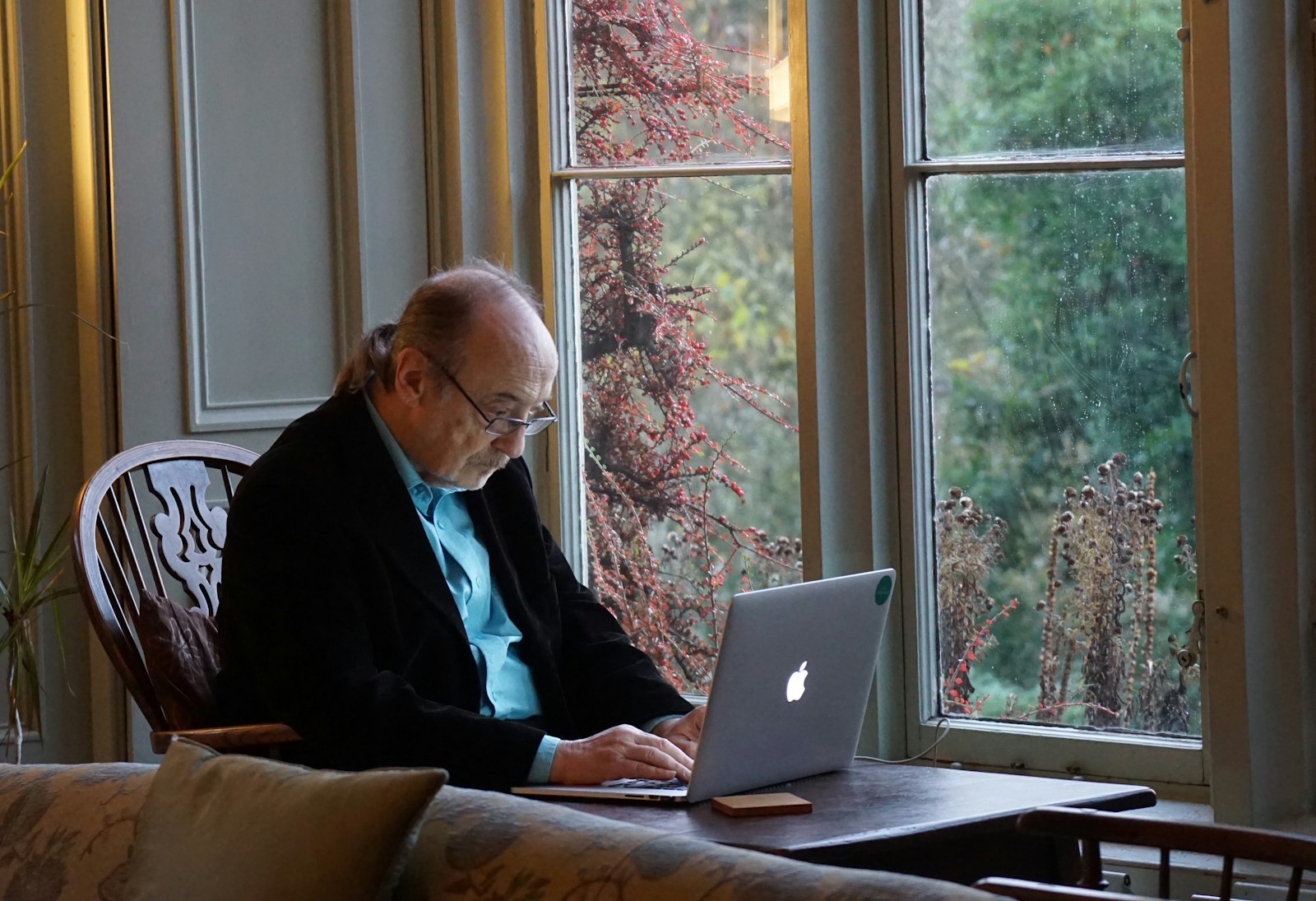 An older man working on a laptop beside a window at home